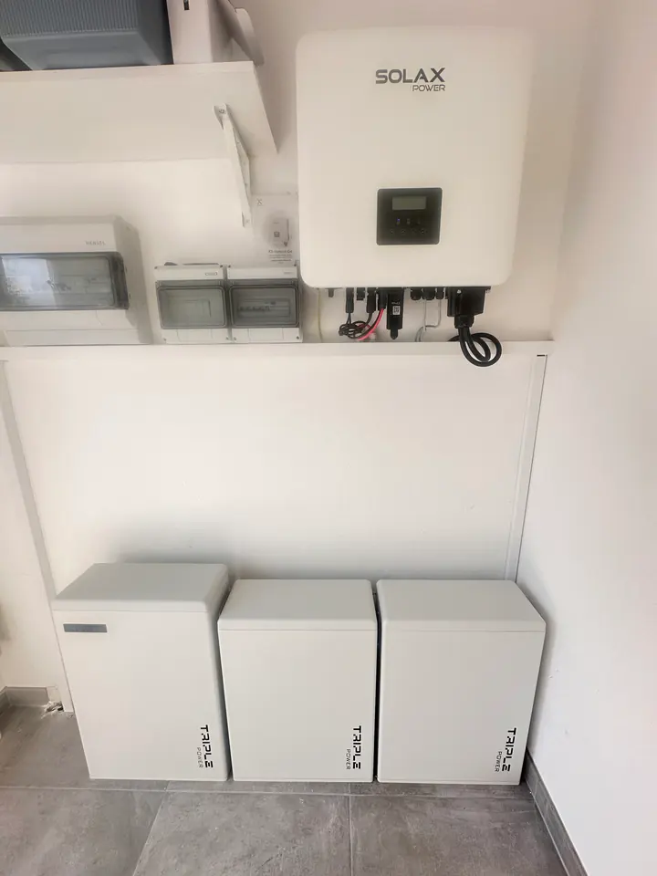 Inversor e três módulos de bateria de armazenamento numa sala técnica, com o quadro elétrico ao lado.