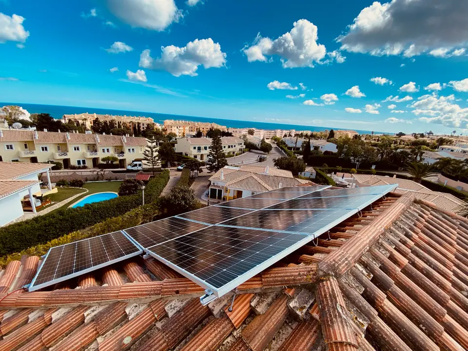 Painéis solares no telhado de uma moradia com piscina, numa urbanização com vista para o mar.